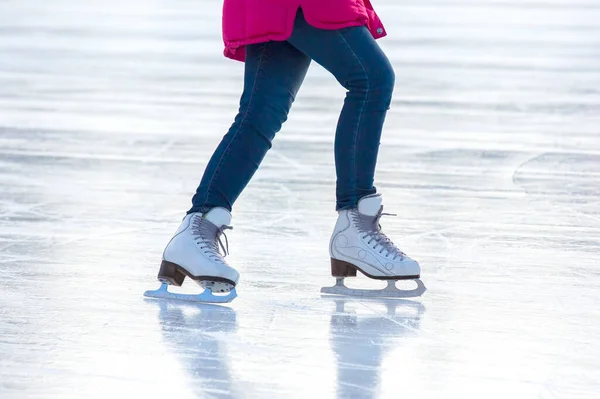 legs of a woman in blue jeans and white skates on an ice rink. hobbies and leisure. winter sports