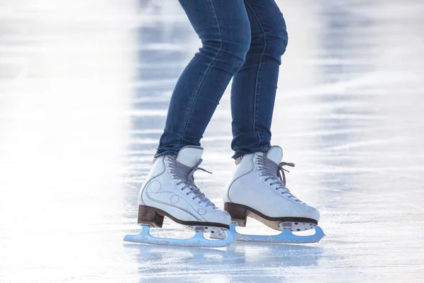 legs of a woman in blue jeans and white skates on an ice rink. hobbies and leisure. winter sport