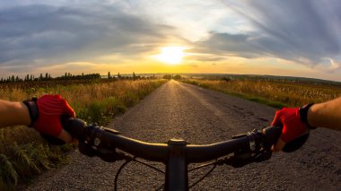 Eller direksiyonda, gün batımına doğru bisiklet sürüyor.