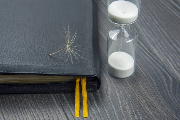 hourglass and bible with dandelion seed. sow the seed of faith in God. Christianity and religion