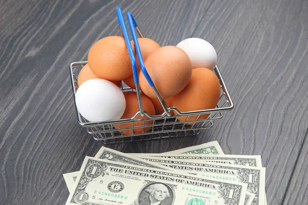 chicken eggs in a supermarket grocery basket against a dollar background on a wooden background. sale and business of food products