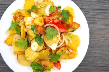 Tahta bir masada, beyaz bir tabakta, sebze ve otlarla pişirilmiş patates kızartması.