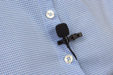 Lavalier mikrofon bir kadın gömleğinin yakın plan klipsiyle korunuyor. Yoğunlaştırıcı mikrofondaki sesin ses kaydı.