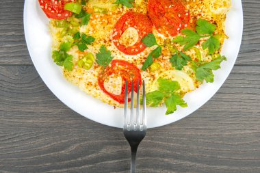 Ahşap bir masada beyaz bir tabakta sebze ve otlarla pişirilmiş omlet.