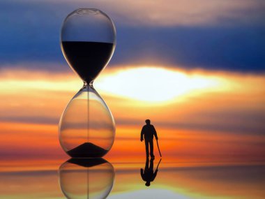 miniature people. silhouette of an elderly man walking towards the sunset next to an hourglass. end of life. clipart