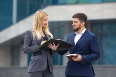 Başarılı iş adamları ortakları bir iş binasının arka planında ellerinde belgelerle iş projesini tartışan kadın ve erkek.