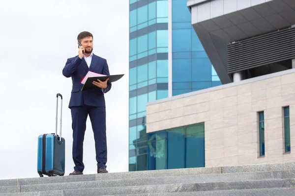Başarılı bir iş adamı, elinde belgelerle bir ofis binasının arka planındaki basamaklarda duruyor.