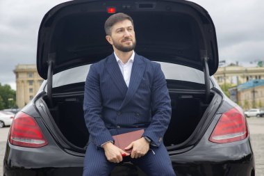 Başarılı iş adamı, prestijli arabasının kaputunda bir günlükle oturuyor.