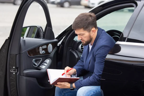 Successful businessman is engaged with documents while sitting near his prestigious car