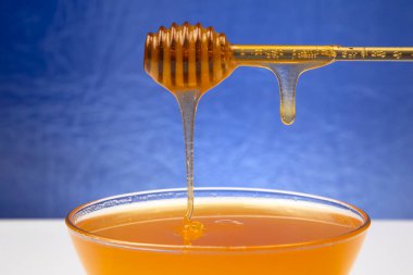 Mavi arka planda bir kaşıktan bir tabağa damlayan taze bal. organik vitamin sağlıklı gıdalar