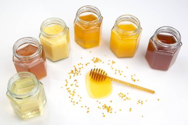 Taze ballı kaşık ve beyaz arka planda farklı bal türleri olan kavanozlar. organik vitamin yiyeceği