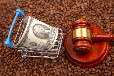 Elinde 2 dolarlık banknotla bir tokmağın yanında oturan kahve çekirdekleri, ticareti, hukuku ve ticareti sembolize ediyor.