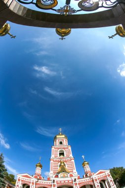 Rus Ortodoks kilisesinin kırmızı ve beyaz çizgili çan kulesinin balık bakışı ve parlak mavi bulutlu bir gökyüzü tarafından çerçevelenmiş altın kubbelerle süslü bir kapı..