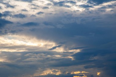 Turuncu, sarı ve koyu mavi tonlarında dramatik bulut oluşumlarıyla gün batımı. Işık ve gölge oyunu büyüleyici bir doğal bileşim yaratır..