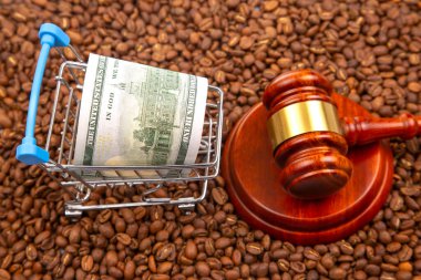 Elinde 2 dolarlık banknotla bir tokmağın yanında oturan kahve çekirdekleri, ticareti, hukuku ve ticareti sembolize ediyor.