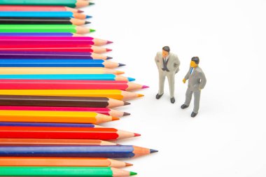 Beyaz bir yüzeye yayılmış renkli kalemler, ayakta duran minyatür işadamları, sanatsal ifade ile kurumsal tasvirleri birleştiriyor. minyatür insanlar