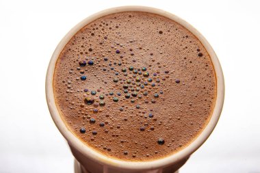 Seramik bir fincanda canlı, yanardöner kabarcıklar olan köpüklü bir kahve yüzeyinin yakın çekimi, zengin kahverengi bir doku ve büyüleyici ışık yansımaları sergiliyor..