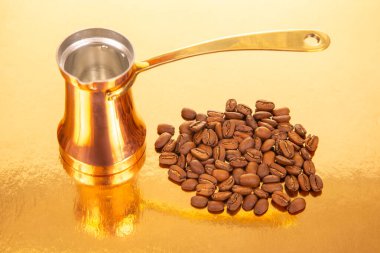 Altın bir arka planda, kahve kültürü ve içecek teması için mükemmel olan kavrulmuş kahve çekirdekleri yanında pirinç saplı parlak bir bakır Türk kahve demliği.
