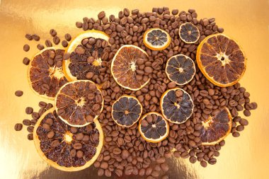 Kavrulmuş kahve çekirdekleri ve altın yansıtıcı bir tabanda kurutulmuş portakal dilimleri, dış görünüş ve sıcaklık. Kahve aroması ve turunçgiller.