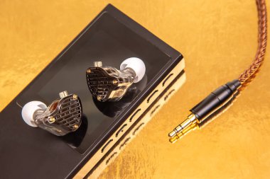 Sade siyah bir müzik çaların üzerinde örülmüş kabloyla kablolu kulaklıklar, altın bir yüzeye yansıyor. Teknoloji, ses ve minimalist tasarım stok fotoğrafçılığı için mükemmel..