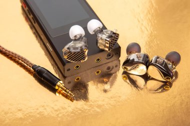 Siyah bir ses çalara bağlı kulaklıklar, altın bir fon, örgülü bir kablo sergiliyor. Teknoloji, ses ekipmanları ve tasarım temaları için harika. Yüksek kaliteli resim.