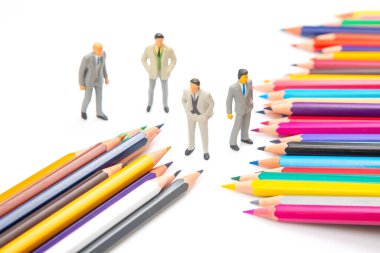 Canlı renkli kalemler beyaz arka planda fan şeklinde dizilmiş ve yanında yaratıcılık ve takım çalışmasını sembolize eden üç küçük iş adamı figürü bulunuyor. minyatür insanlar