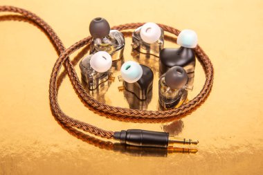 Üç çift kablosu örgülü kulaklık ve yansıtıcı altın bir yüzeye 3.5 mm fiş, teknoloji ve ses donanımı teması için ideal..