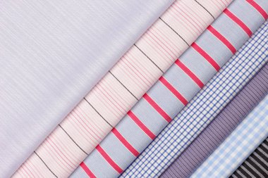 Bir tekstil dükkanında düzgünce düzenlenmiş çeşitli kumaşlardan oluşan bir koleksiyon. Çizgiler ve çekler de dahil olmak üzere parlak renkler ve desenler görünür, moda tasarımcıları ve hobiciler için aynı çekicilikte.