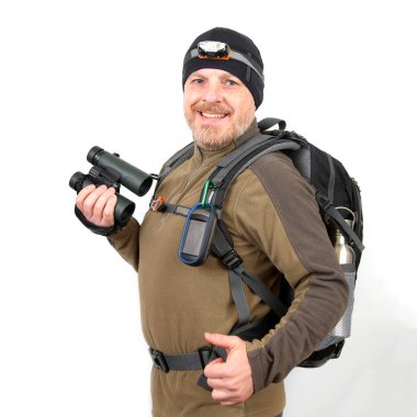 Bir adam açık hava malzemeleriyle dolu bir sırt çantası takmış gülümsüyor. Elinde dürbün tutuyor ve doğada keşif ve maceraya hazır bir far takıyor..