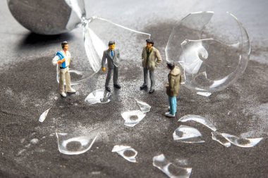 Kırık cam parçalarıyla çevrili karanlık bir yüzeyde duran dört minyatür figür kırılgan kalıntılarla beklenmedik karşılaşmalarını tartışıyor. Atmosfer gerilimi ve şaşkınlığı gösterir..