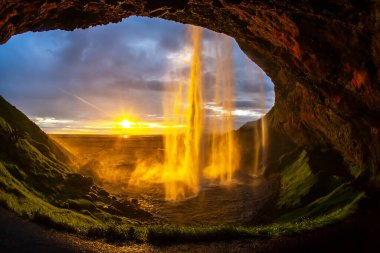 Güneş İzlanda 'da batarken kayalık bir mağaradan çarpıcı bir şelale akar ve suyun ve çevrenin üzerine altın renkler serer. Manzara huzuru ve doğal güzelliği çağrıştırıyor..