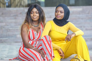 İki Afrikalı kadın, şık kıyafetlerini sergileyerek dışarıda rahatlar..
