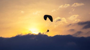 Güneş batarken bulutların üzerinde zarif bir şekilde süzülen bir paraglider gökyüzünde sıcak renkler bırakıyor. Huzurlu sahne, maceranın güzelliğini ve uçmanın heyecanını yakalar..