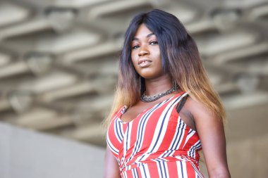 Afrikalı bir kadın kendine güvenerek şık çizgili elbisesini sergiliyor. Arka planda modern mimari yer alıyor. Benzersiz moda anlayışı ile canlı bir tezat oluşturuyor..