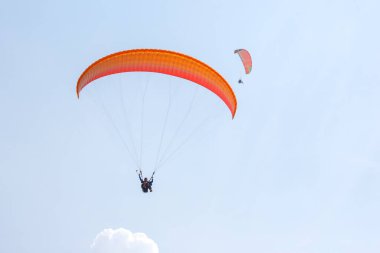 İki yamaç paraşütçüsü açık mavi gökyüzünde süzülerek güneşli bir günde, yumuşak bulutlarla çevrili ve aşağıdaki geniş manzaranın tadını çıkarırlar..