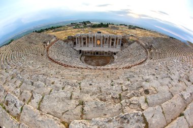 Ziyaretçiler, Türkiye 'nin Hierapolis kentindeki antik amfitiyatronun etkileyici mimarisine ve tarihsel önemine hayret ederek manzaranın üzerinde güzel bir gün batımının keyfini çıkarabiliyorlar..