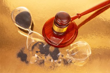 Bir tokmak, yansıtıcı altın bir yüzeye uzanır. Kırık bir kum saatinin yanında, siyah kumlar dökülür. Bu kompozisyon adalet, zaman ve kararların kırılganlığını temsil eder..