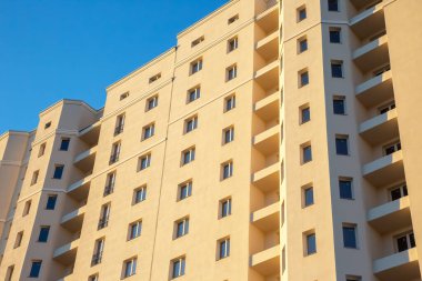 Yeni inşa edilen bir apartmanda çok sayıda balkonu olan bej bir cephe yer alıyor. Parlak mavi gökyüzü, hava kararmaya başladığında mimarinin temiz çizgilerini güçlendirir..