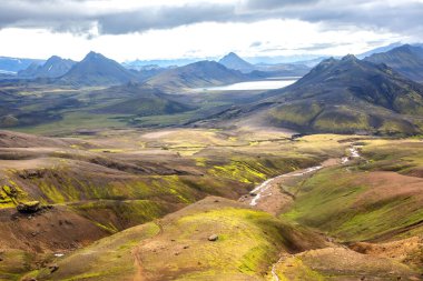 İzlanda 'nın engebeli yabanın nefes kesen manzarası geniş dağları, uzakta sakin bir gölü ve bulutlu bir gökyüzünün altında yemyeşil vadileri kesen dolambaçlı bir nehri gözler önüne serer..