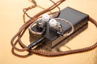 Parlak bir yüzeyde, ses teknolojisi ve tasarım unsurlarını gösteren, kulaklıklı birinci sınıf ses oynatıcısı, ses deneyiminin karmaşıklığını vurguluyor..