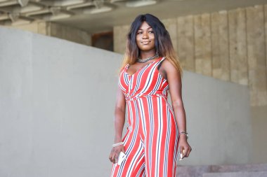 Afrika kökenli bir kadın şık çizgili bir tulumla şık bir şekilde duruyor, şehir ortamında duruşunu sergiliyor..