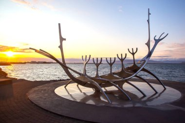Bir Viking gemisini temsil eden modern bir heykel, İzlanda 'nın Reykjavik kentinde canlı bir günbatımının arka planında görkemli bir şekilde duruyor. Ziyaretçiler bu sanatsal övgüye hayran..