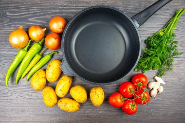 Taze sebzelerin bir çeşidi ahşap bir masada bir pişirme tavasının yanında sergilenir. Patates, soğan, domates, sarımsak ve yeşil biber hazır..