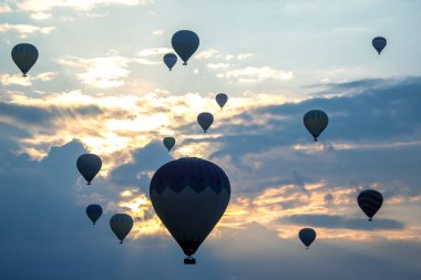 Renkli sıcak hava balonları güneş doğarken Cappadocia 'nın üstündeki gökyüzünü dolduruyor. Bulutların ve yumuşak güneş ışığının altında parladığı yere doğru nefes kesici bir manzara yaratıyor..