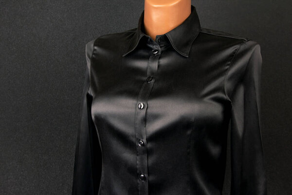 A sleek black satin button-up shirt is showcased on a mannequin against a dark backdrop, highlighting its glossy finish and stylish design. Ideal attire for formal events or chic casual wear.