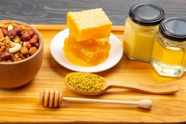Çeşit çeşit fındık ve çeşitli kurutulmuş narenciye meyveleri ve mutfak tahtasının üzerinde taze bal peteği ve polen. İnsan vücudu için yararlı vitamin yiyeceği