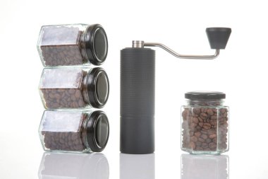 Kahve çekirdekleri için siyah manuel kahve öğütücüsü ve siyah kahve çekirdekleri ile dolu dört cam şeffaf kavanoz ve beyaz arka planda kahve demlemek için toprak takımı. Kahve için mutfak aletleri..