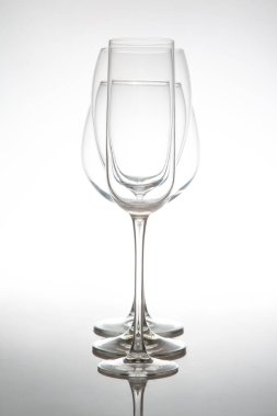 Uzun saplı üç zarif, boş şarap kadehinden oluşan gösterişli bir sıra, yumuşak gri arka planda parlak bir yüzeye yansıyor, yemek ya da olay temaları için mükemmel..