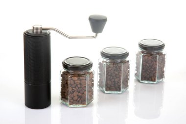 Kahve çekirdekleri için siyah manuel kahve öğütücüsü ve siyah kahve çekirdekleri ile dolu üç bardak şeffaf kavanoz ve beyaz arka planda kahve demlemek için toprak takımı. Kahve için mutfak aletleri..