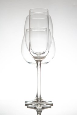 Uzun saplı üç zarif, boş şarap kadehinden oluşan gösterişli bir sıra, yumuşak gri arka planda parlak bir yüzeye yansıyor, yemek ya da olay temaları için mükemmel..